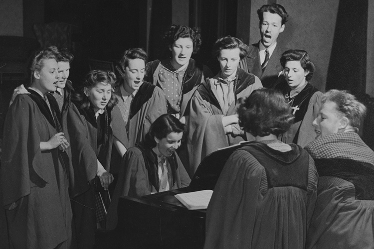 gowned students, mostly female, around piano, c.1950-55