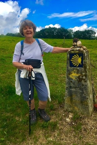 Woman in hiking clothes standing by milestone for Camino de Santiago