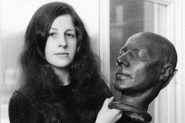 Woman with long, dark hair, holding a sculpted male head.