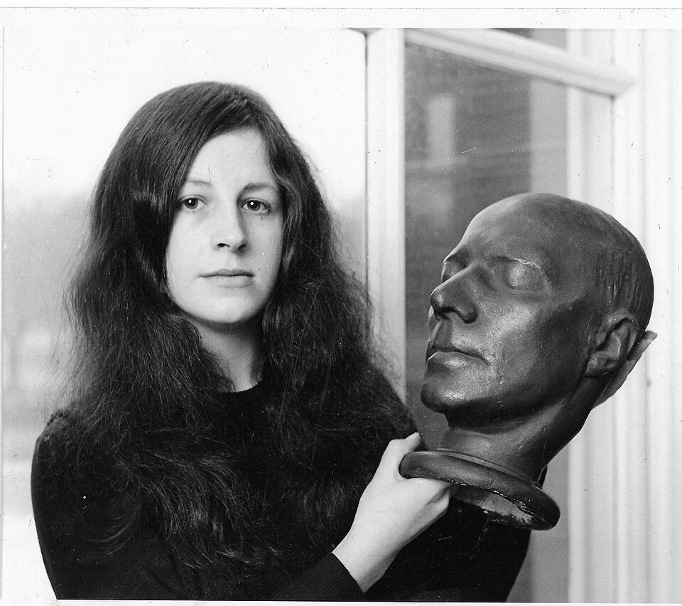 Woman with long, dark hair, holding a sculpted male head.